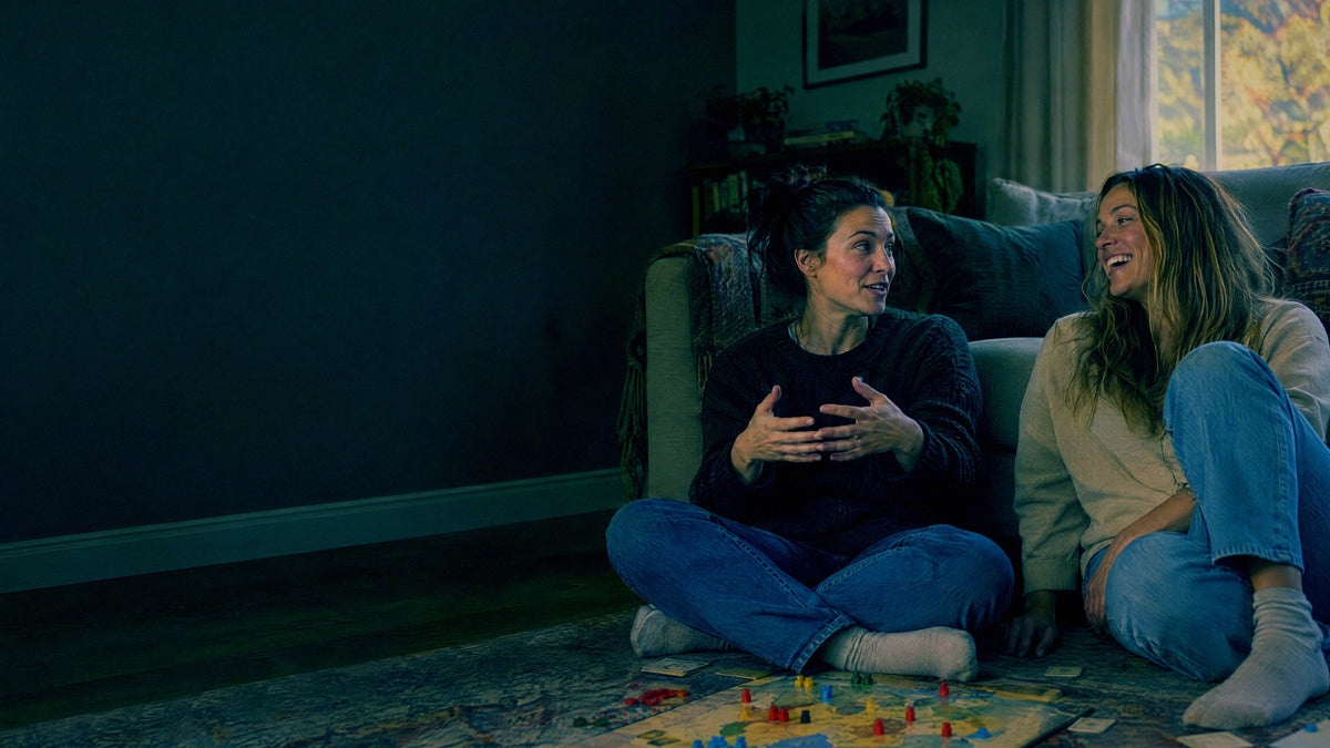 Two sisters sit on the living room floor mid conversation with a half finished board game