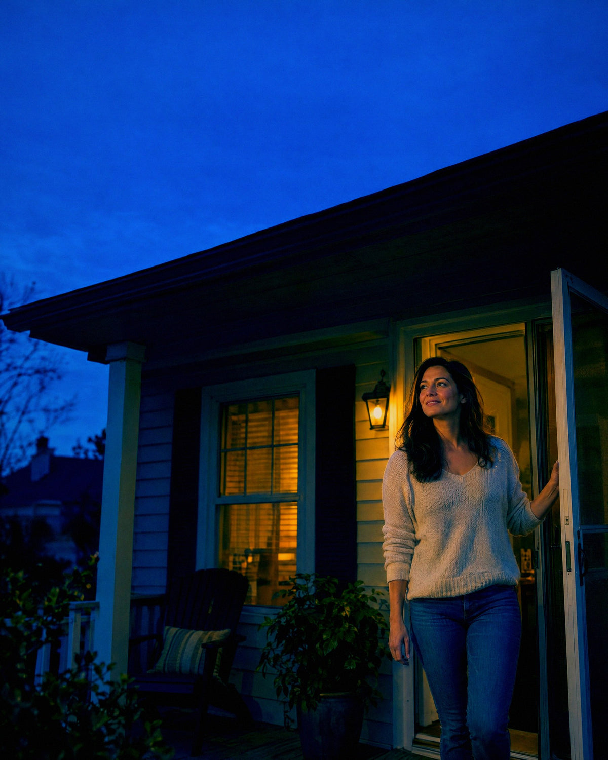 A woman steps out onto her porch in the early evening and looks up the street